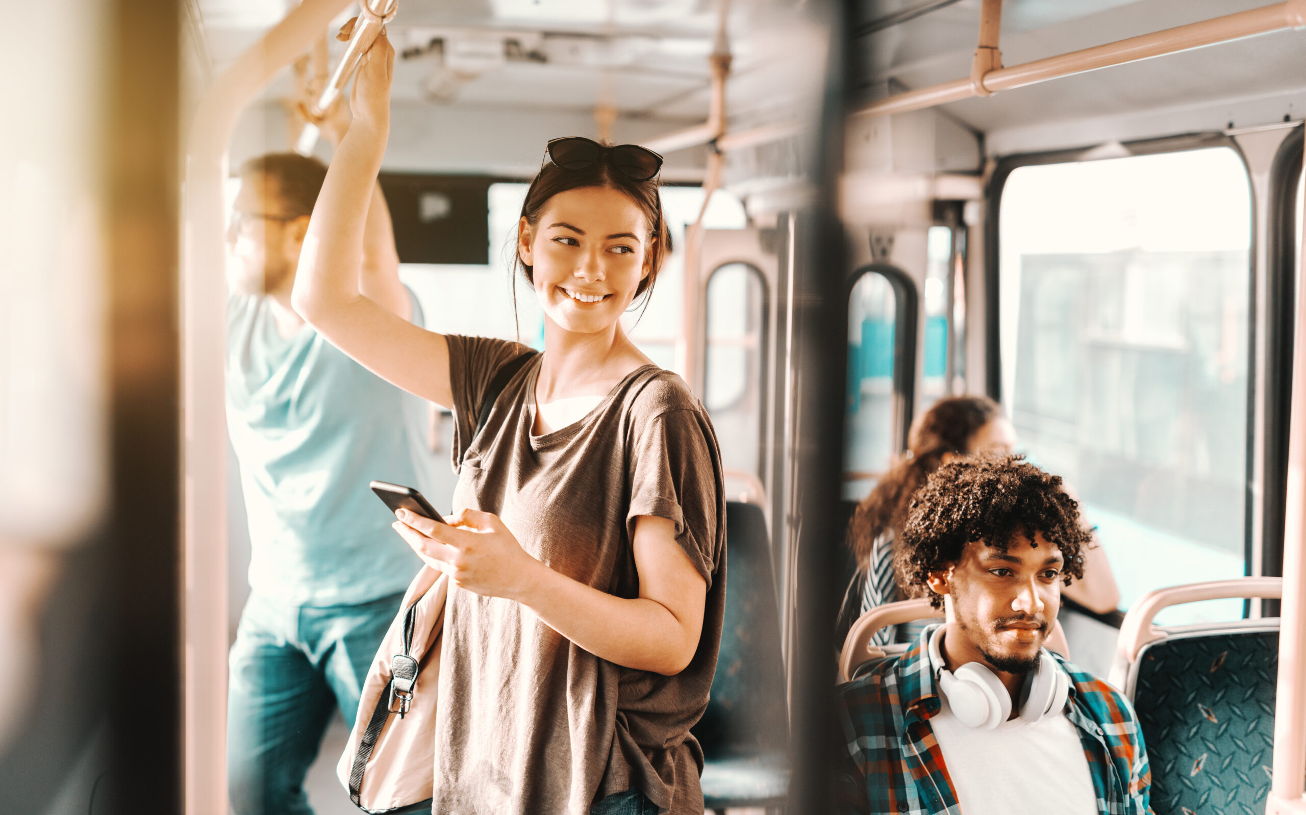 Eine junge Frau, die lächelnd im Bus steht, sich seitlich dreht mit Smartphone in der Hand Eine junge Frau, die lächelnd im Bus steht, sich seitlich dreht mit Smartphone in der Hand